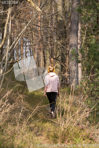 Image of Rear view of active sporty woman listening to the music while running in autumn fall forest. Female runner training outdoor. Healthy lifestyle image of young caucasian woman jogging outside