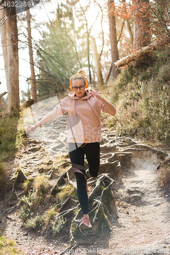 Image of Active sporty woman running in autumn fall forest jumping over the roots on the path. Healthy lifestyle image of young active caucasian woman jogging outside in nature