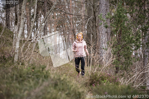 Image of Active sporty woman listening to the music while running in autumn fall forest. Female runner training outdoor. Healthy lifestyle image of young caucasian woman jogging outside