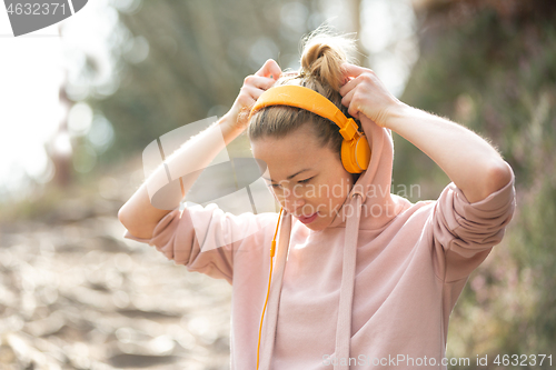 Image of Portrait of beautiful sports woman with hoodie and headphones during outdoors training session.