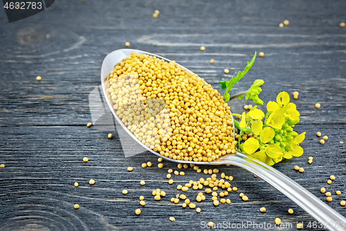 Image of Mustard seeds in metal spoon with flower on board