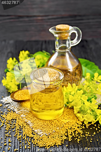 Image of Oil mustard in jar and decanter with flower on dark wooden board