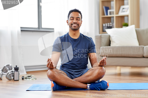 Image of indian man meditating in lotus pose at home