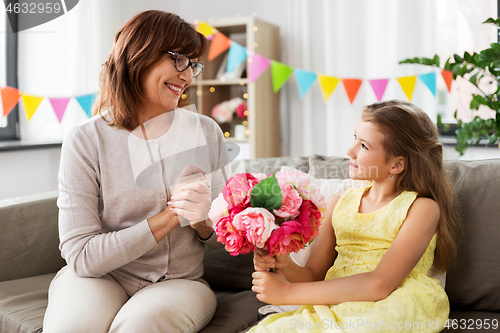 Image of granddaughter giving grandmother flowers at home