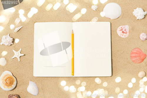 Image of notebook with pencil and seashells on beach sand