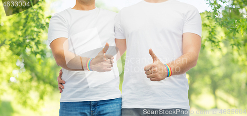 Image of gay couple with rainbow wristbands shows thumbs up