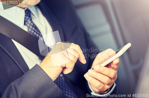 Image of senior businessman texting on smartphone in car