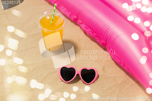 Image of sunglasses, juice and pool mattress on beach sand