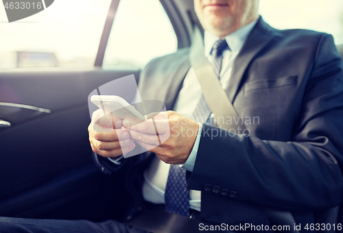 Image of senior businessman texting on smartphone in car