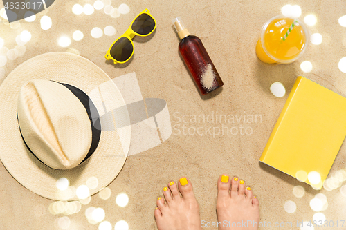 Image of feet, hat, shades, sunscreen and juice on beach