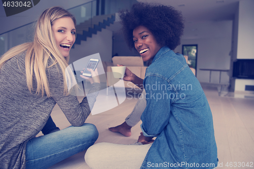 Image of young multiethnic women sit on the floor and drinking coffee