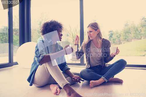 Image of multiethnic women sit on the floor and drinking coffee
