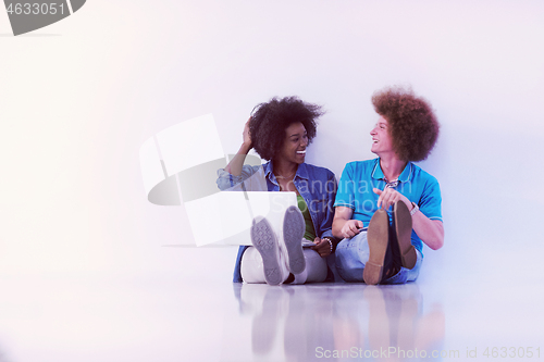 Image of multiethnic couple sitting on the floor with a laptop and tablet