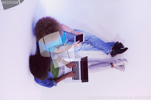 Image of multiethnic couple sitting on the floor with a laptop and tablet