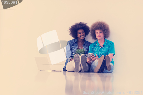 Image of multiethnic couple sitting on the floor with a laptop and tablet