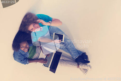 Image of multiethnic couple sitting on the floor with a laptop and tablet