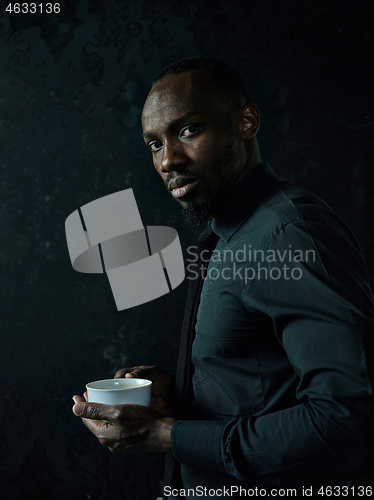 Image of Stylish young black man with cup of coffee posing on dark background.