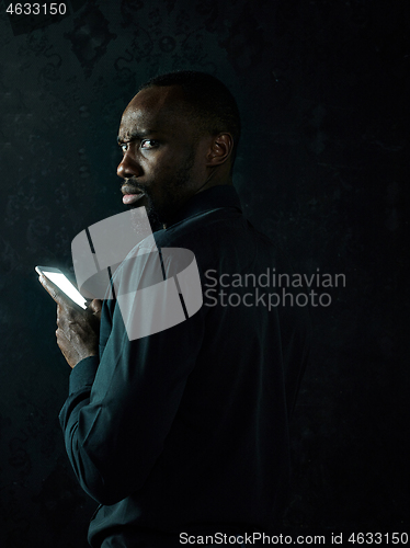 Image of Studio shot of young serious black African man thinking while talking on mobile phone against black background