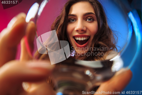 Image of The surprised young woman in party clothes posing with glass of wine.