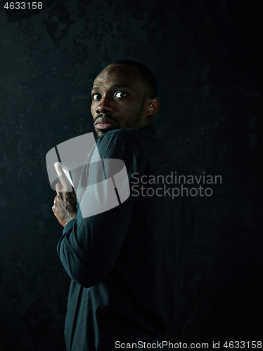 Image of Studio shot of young serious black African man thinking while talking on mobile phone against black background