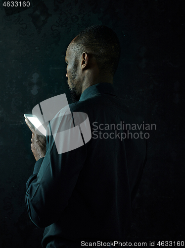 Image of Studio shot of young serious black African man thinking while talking on mobile phone against black background
