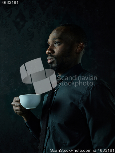 Image of Stylish young black man with cup of coffee posing on dark background.