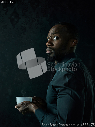 Image of Stylish young black man with cup of coffee posing on dark background.