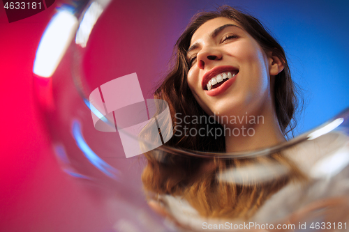 Image of The surprised young woman in party clothes posing with glass of wine.