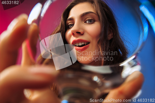 Image of The surprised young woman in party clothes posing with glass of wine.