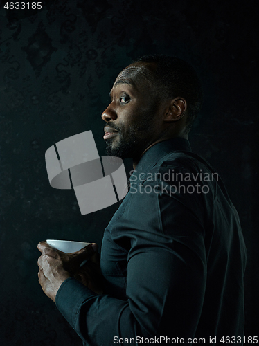 Image of Stylish young black man with cup of coffee posing on dark background.