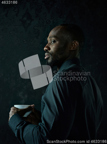 Image of Stylish young black man with cup of coffee posing on dark background.