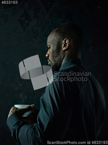 Image of Stylish young black man with cup of coffee posing on dark background.