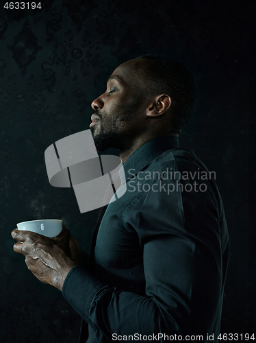 Image of Stylish young black man with cup of coffee posing on dark background.