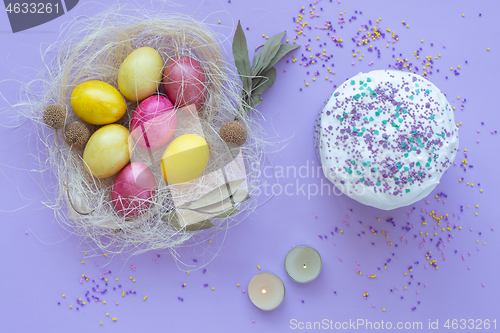 Image of Easter eggs in the nest, cake, candles on a purple background
