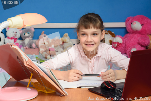 Image of The girl in the children\'s room sits at the desk with a smile and does her homework