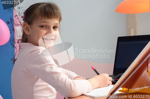 Image of Girl in good spirits doing homework at the desk at home