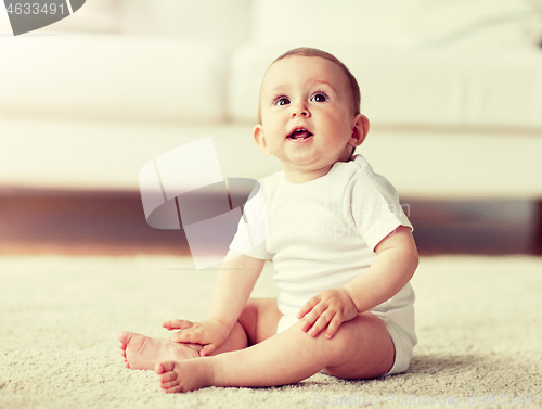 Image of happy baby boy or girl sitting on floor at home