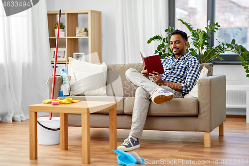 Image of man reading book and resting after home cleaning