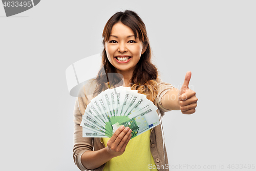 Image of asian woman with euro money showing thumbs up