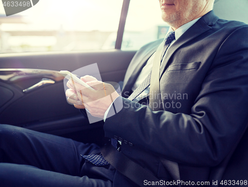 Image of senior businessman texting on smartphone in car