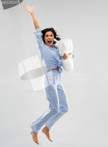 Image of happy woman in blue pajama jumping with pillow