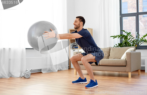 Image of man exercising and doing squats with ball at home