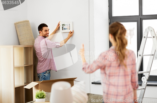 Image of happy couple moving to new home and hanging photo