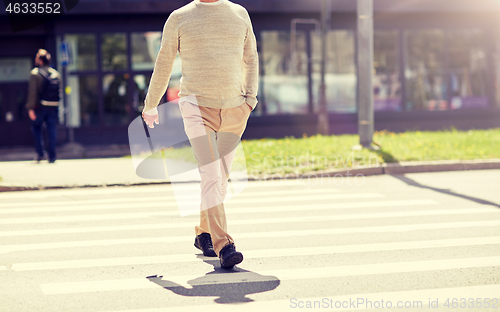 Image of senior man walking along city crosswalk