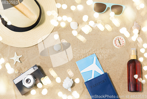 Image of travel tickets, camera and hat on beach sand