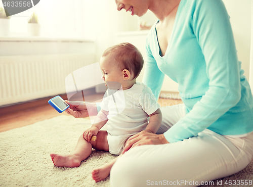 Image of happy mother showing smartphone to baby at home