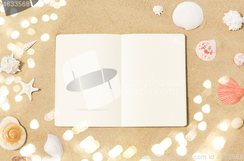 Image of notebook with seashells on beach sand