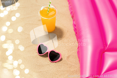 Image of sunglasses, juice and pool mattress on beach sand