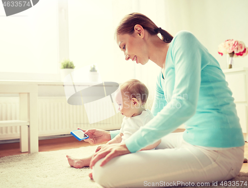 Image of happy mother showing smartphone to baby at home