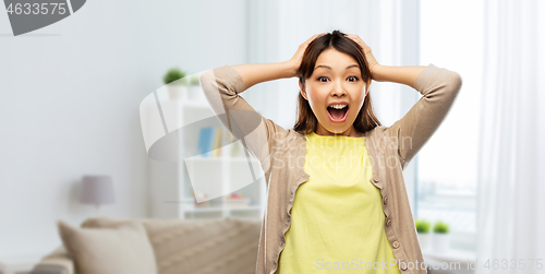 Image of happy asian woman holding to her head at home